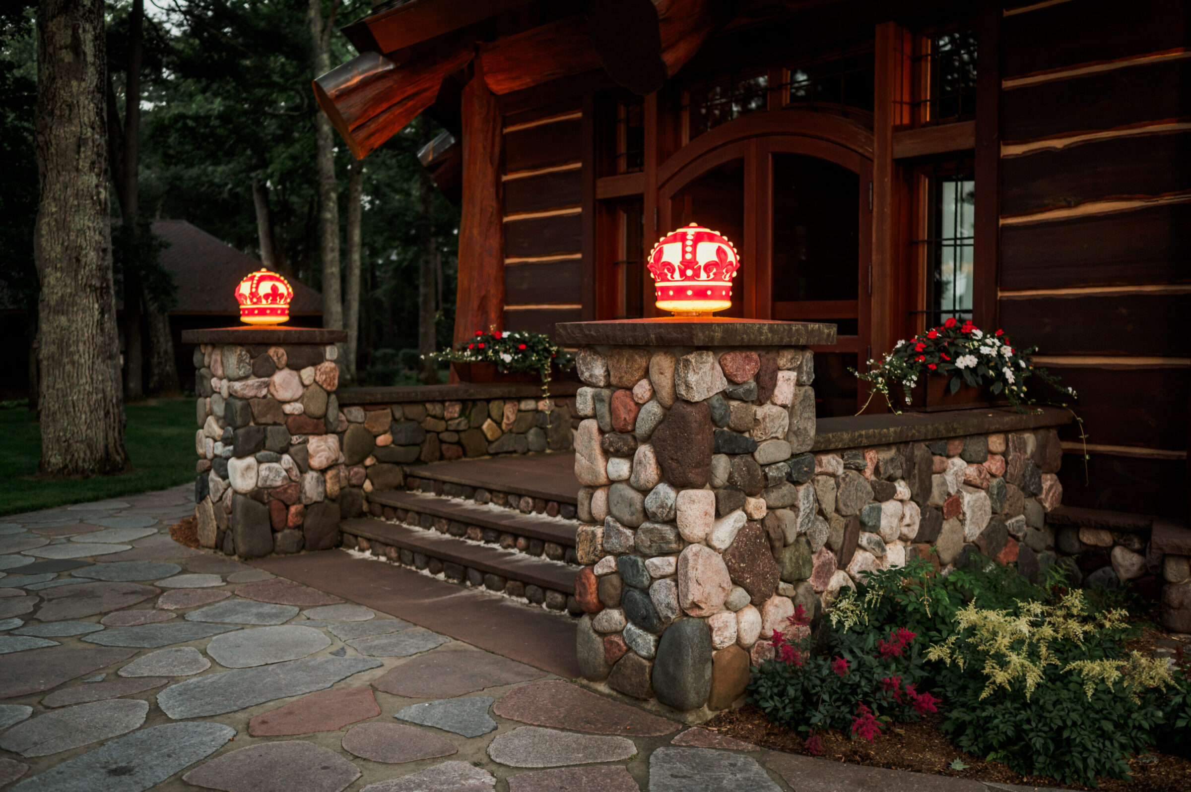 Two illuminated red crown lanterns on stone pillars flanking a log cabin entrance.