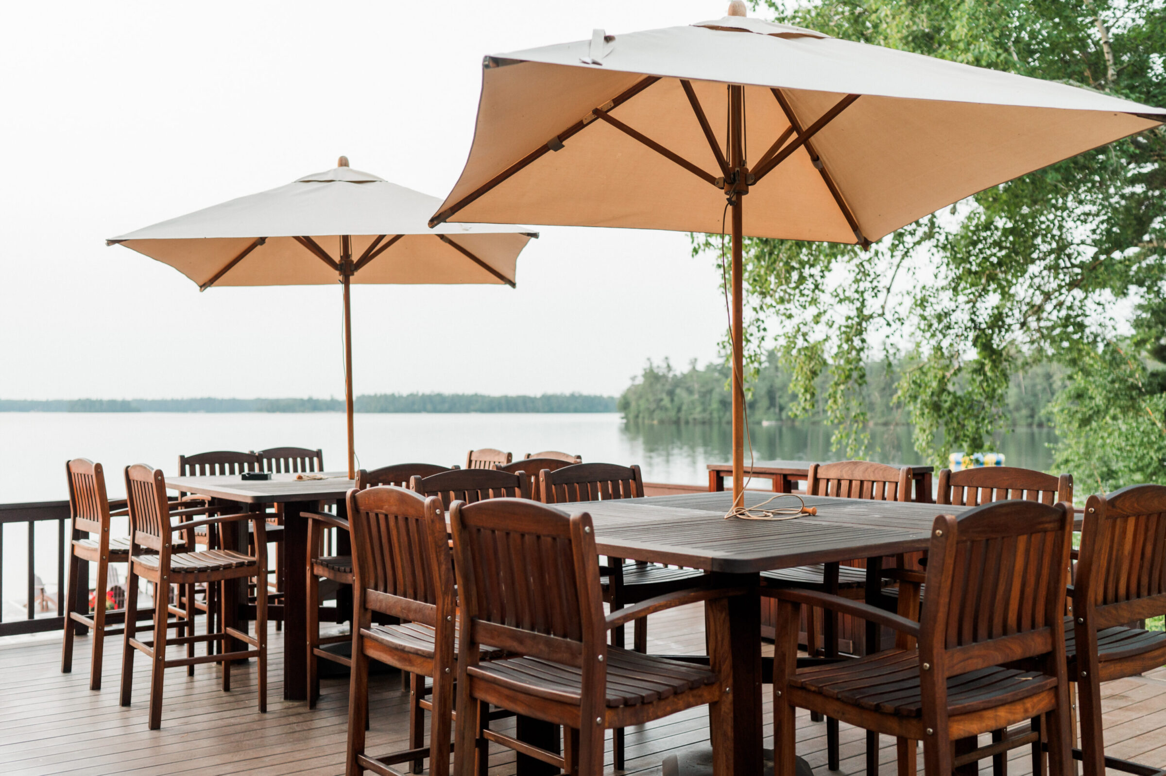 Outdoor dining tables and chairs with umbrellas on a deck overlooking a lake.