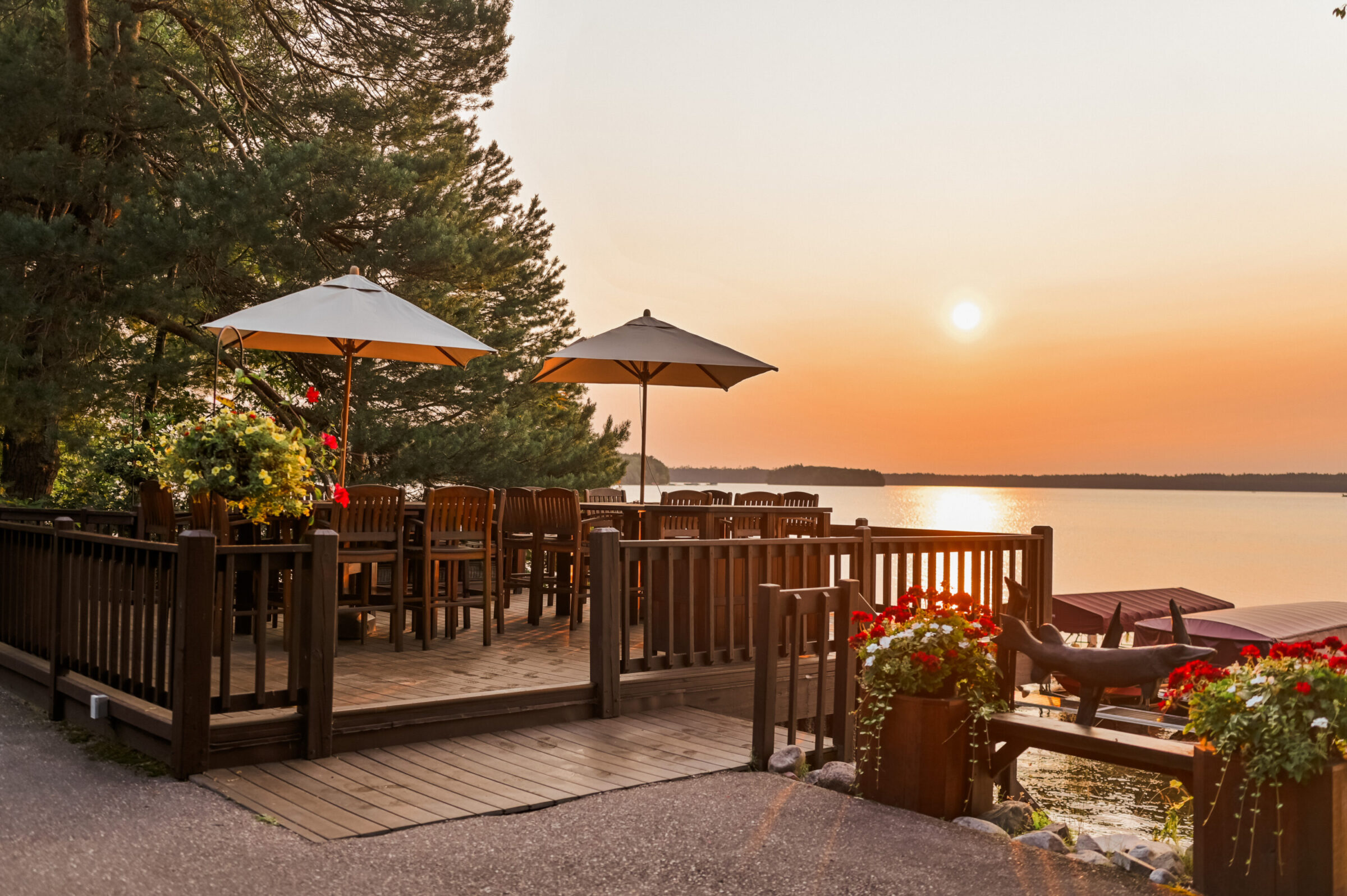 Deck with tables, umbrellas, and lake view at sunset.